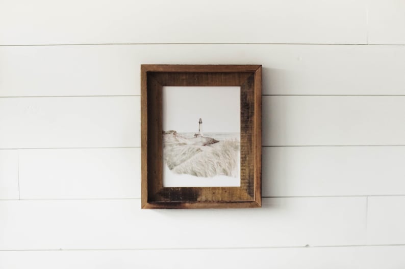 May include: A framed watercolor painting of a lighthouse on a sandy beach with tall grass in the foreground.
