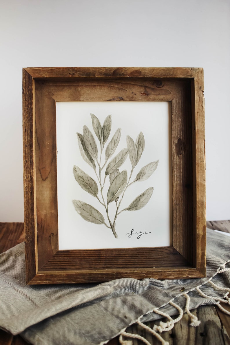May include: A framed watercolour painting of a sage plant with green leaves. The frame is made of rustic wood and has a white mount. The word "Sage" is written in cursive at the bottom of the painting.