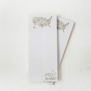 May include: Two white lined notepad sets with a floral design of the United States map on the top. The bottom of the notepad says "America is beautiful".