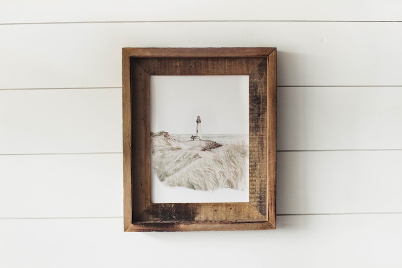 May include: A framed print of a lighthouse on a grassy hill overlooking the ocean. The print is in a rustic wooden frame.