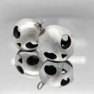 May include: Two silver earrings shaped like a face with cut-out eyes, nose, and mouth.