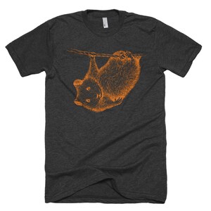 May include: A dark heather grey t-shirt with an orange illustration of a possum hanging upside down from a branch.