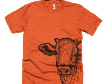 May include: Orange t-shirt with a black and white illustration of a cow's head on the right side of the shirt.