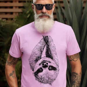 Puede incluir: Una camiseta rosa con una ilustración en blanco y negro de un perezoso colgado boca abajo. El perezoso tiene una cara detallada con ojos grandes.