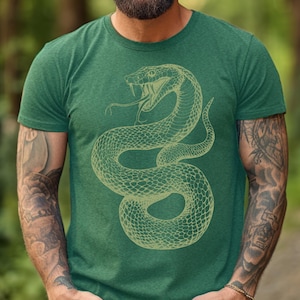 Pode incluir: Uma camiseta verde com um contorno amarelo de uma cobra enrolada com a boca aberta. A cobra tem um padrão texturizado.