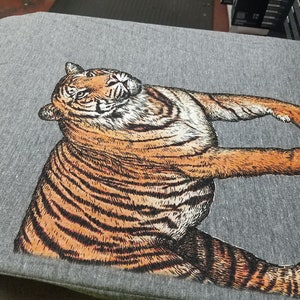 May include: A gray t-shirt with a black and orange tiger illustration printed on the front.