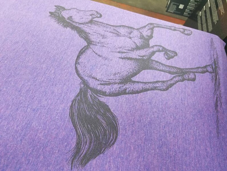 May include: A purple t-shirt with a black and white image of a horse rearing up on its hind legs.