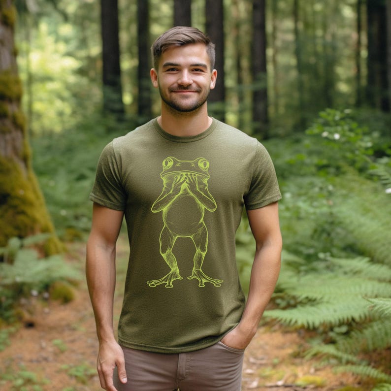 May include: A green t-shirt with a yellow outline of a frog covering its eyes with its hands.