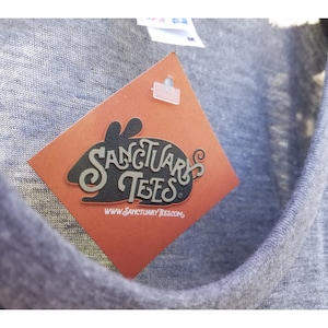 May include: A gray t-shirt with a red tag attached. The tag has a black silhouette of a rabbit with the text "Sanctuary Tees" and the website "www.sanctuarytees.com".