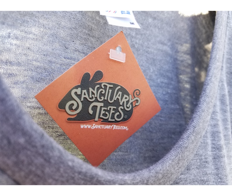 May include: A gray t-shirt with a red tag attached. The tag has a black silhouette of a rabbit with the text "Sanctuary Tees" and the website "www.sanctuarytees.com".
