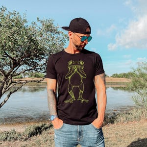 May include: A black t-shirt with a yellow graphic of a frog covering its eyes with its hands.