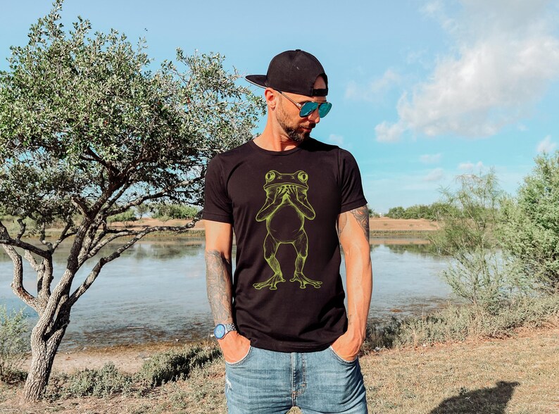May include: A black t-shirt with a yellow graphic of a frog covering its eyes with its hands.