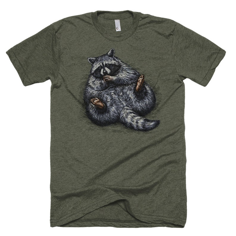 May include: A green t-shirt with a graphic of a raccoon curled up in a ball. The raccoon is gray and black with a white stripe on its face.