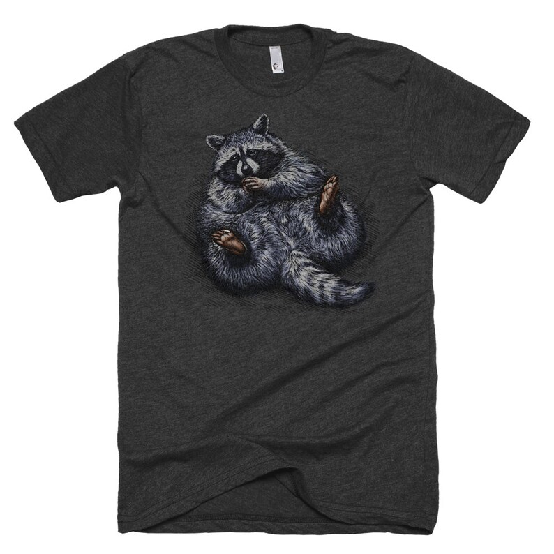 May include: A dark heather grey t-shirt with a graphic of a raccoon curled up in a ball. The raccoon is grey and black with a white face and black eyes.