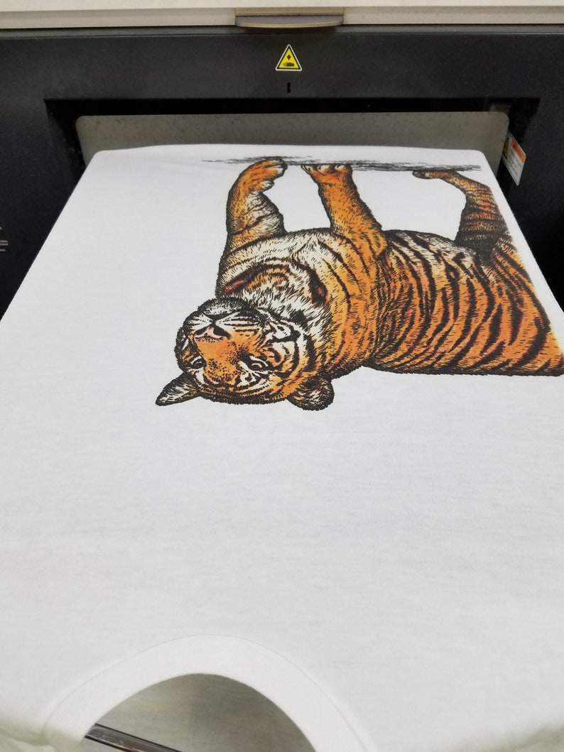 May include: A white t-shirt with a black and orange tiger print. The tiger is upside down and appears to be looking at the camera.