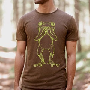 May include: A brown t-shirt with a yellow outline of a frog covering its eyes with its hands.