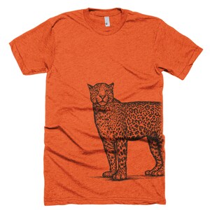 May include: Orange t-shirt with a black and white illustration of a leopard on the right side of the shirt.