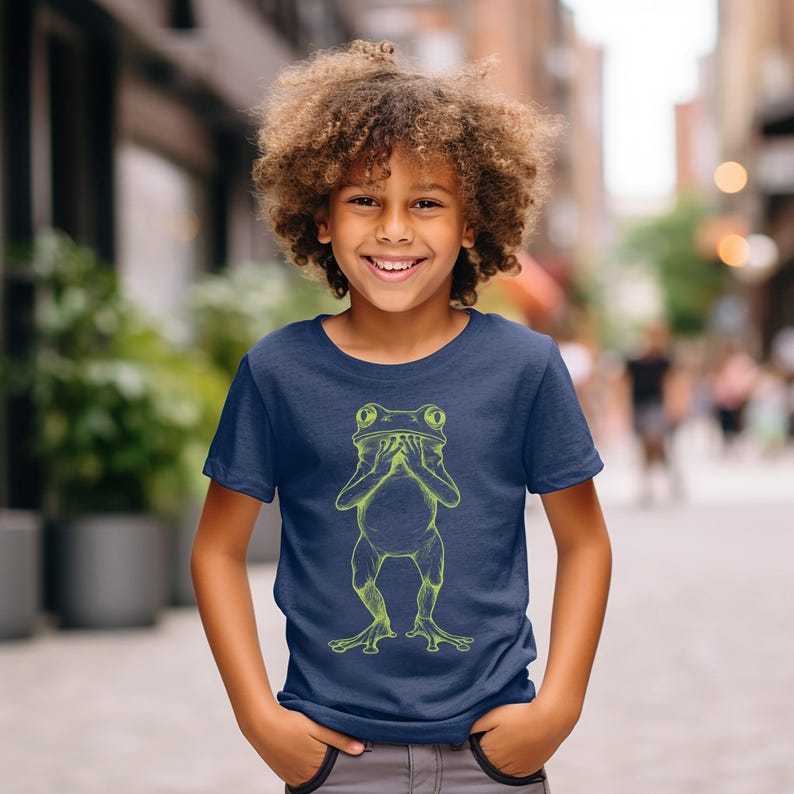 May include: A young person wearing a navy blue t-shirt with a lime green illustration of a frog covering its eyes with its hands.