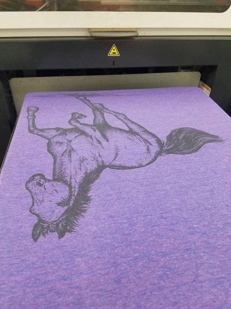 May include: A purple t-shirt with a black and white image of a horse rearing up on its hind legs.