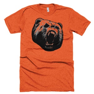 May include: Orange t-shirt with a black and white graphic of a bear's head with its mouth open.