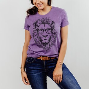 May include: Purple t-shirt featuring a graphic of a lion wearing glasses. The lion is black and white and the shirt is a heather purple colour.