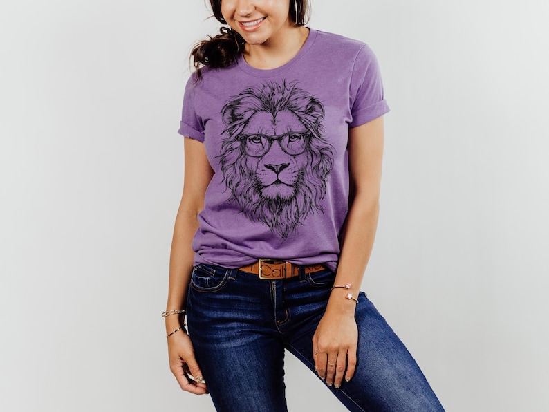 May include: Purple t-shirt featuring a graphic of a lion wearing glasses. The lion is black and white and the shirt is a heather purple colour.