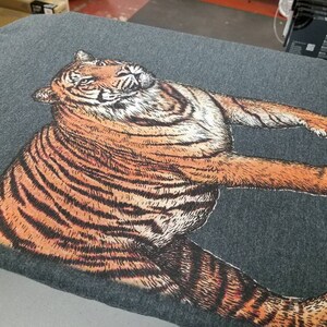 May include: A gray t-shirt with a detailed illustration of a tiger printed on the front. The tiger is facing to the right and has orange and black stripes.