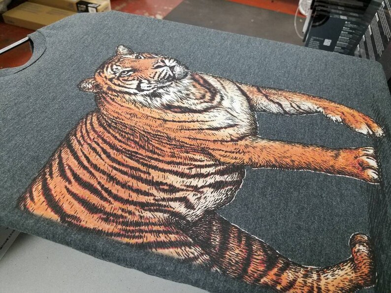 May include: A gray t-shirt with a detailed illustration of a tiger printed on the front. The tiger is facing to the right and has orange and black stripes.