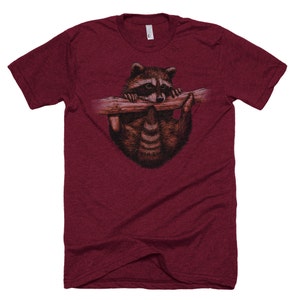 Puede incluir: Una camiseta de color granate con un gr&aacute;fico de un mapache colgado de una rama y mirando hacia abajo.