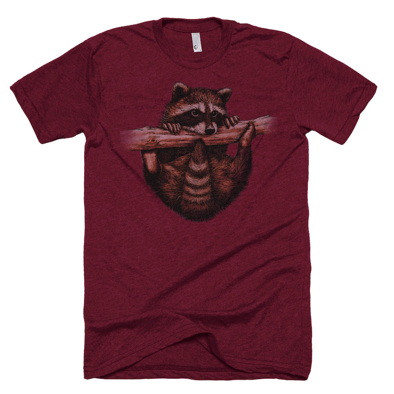 Puede incluir: Una camiseta de color granate con un gr&aacute;fico de un mapache colgado de una rama y mirando hacia abajo.