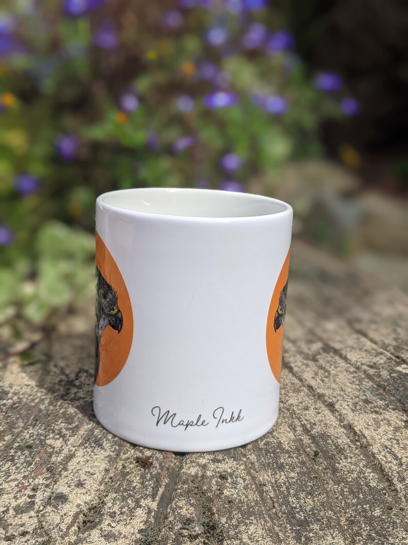 May include: White ceramic mug with an orange circle and a black and white bird illustration. The mug has the text "Maple Inkk" printed on the bottom.