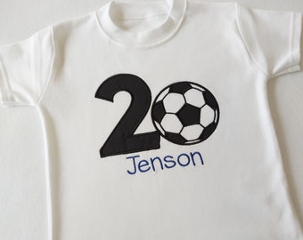 Puede incluir: Camiseta blanca con el número 20 en negro y un balón de fútbol. El nombre "Jenson" está bordado en azul. La camiseta está hecha de una tela suave y clara.