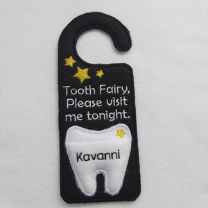 May include: Black felt door hanger with a white tooth shape and the text "Tooth Fairy, Please visit me tonight."  The tooth has a gold star and the name "Kavanni" written inside.