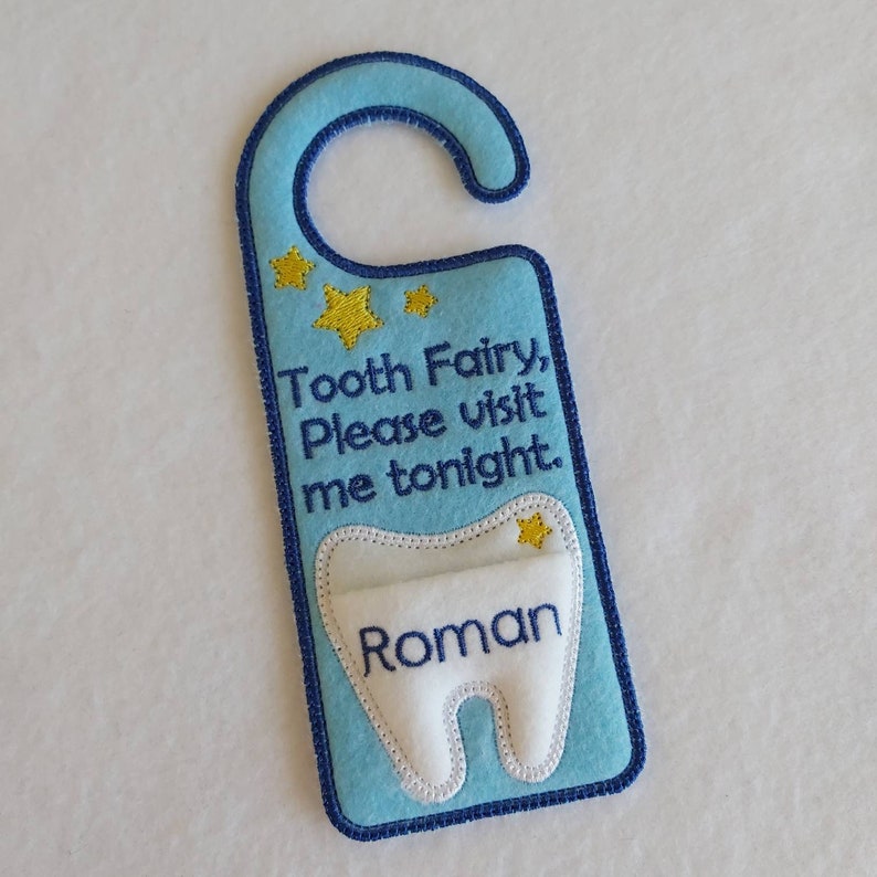 May include: Blue felt tooth fairy door hanger with a white felt tooth pocket and the text "Tooth Fairy, Please visit me tonight." and the name "Roman" embroidered on the tooth.
