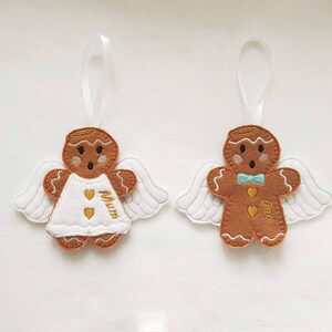 Puede incluir: Dos adornos de &aacute;ngeles de pan de jengibre con alas blancas y cintas para colgar. Un &aacute;ngel viste un vestido blanco con "Mum" bordado en dorado, el otro tiene una pajarita azul y "Dad" bordado en dorado. Decoraci&oacute;n navide&ntilde;a festiva.