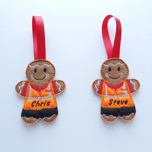 May include: Two gingerbread man Christmas tree decorations with red ribbon hangers. Each is brown with a smiling face and wears an orange vest and black trousers. One says "Chris" and the other says "Steve".