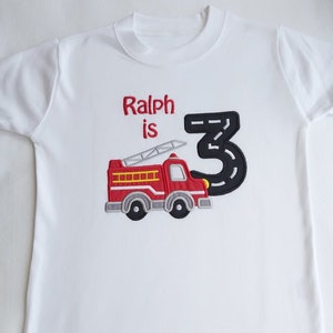 May include: White t-shirt with red and black embroidered fire truck and the text "Ralph is 3" on it.
