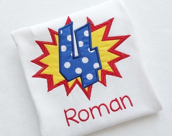 May include: White t-shirt with a red, yellow, and blue embroidered design of the number four with white polka dots. The name "Roman" is embroidered in red below the design.