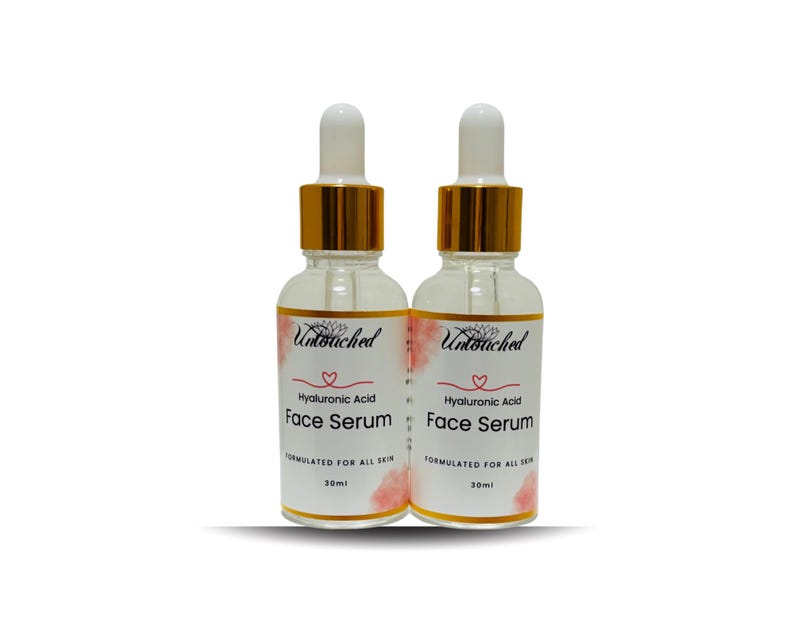 May include: Two clear glass bottles of face serum with white droppers and gold-colored collars. Each bottle has a label with the text "Untouched", "Hyaluronic Acid Face Serum", and "FORMULATED FOR ALL SKIN". The bottles are 30ml each.