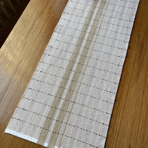 Peut inclure: Un chemin de table beige avec deux bandes brunes au centre. Le chemin de table a une bordure blanche et un motif en chevrons subtil.