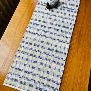 Peut inclure: Un chemin de table blanc avec un motif à carreaux bleus, jaunes et blancs. Un leurre de canard en bois est placé sur le chemin de table.