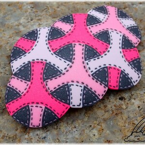 May include: Three pink, white, and gray polymer clay circles with a geometric pattern. The circles are arranged in a stack, with the largest circle on the bottom and the smallest circle on top. The circles have a stitched design around the edges.