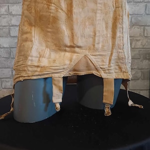 May include: A beige garter belt with floral pattern and elastic straps. The garter belt is displayed on a mannequin.