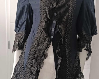 May include: A black blouse with a high collar and lace trim. The lace is ruffled and has a beaded design. The blouse has a button-up front.
