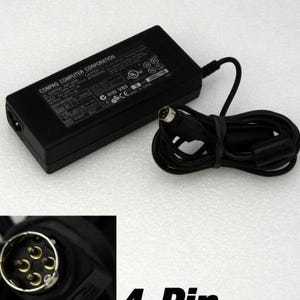May include: A black rectangular AC power adapter brick labeled COMPAQ COMPUTER CORPORATION with an attached black power cord ending in a 4-pin circular connector. The adapter features technical specifications and safety certification symbols printed on its surface.
