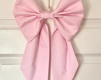 May include: A large pink bow with long tails hanging from a hook on a white door.