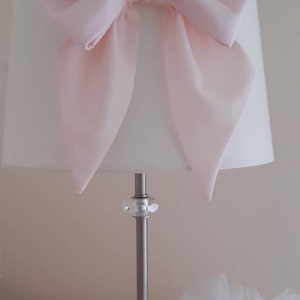 May include: A white lampshade with a large pink bow on top. The lamp has a silver base with a clear crystal accent.
