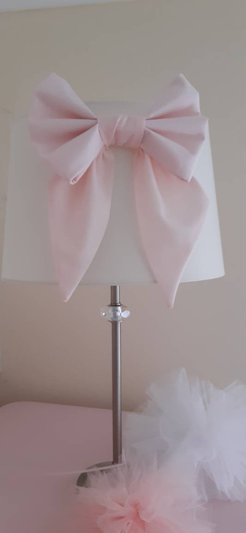 May include: A white lampshade with a large pink bow on top. The lamp has a silver base with a clear crystal accent.