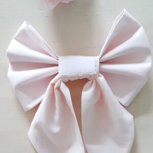 May include: A pale pink fabric bow with two long tails, tied with a white velcro strip.
