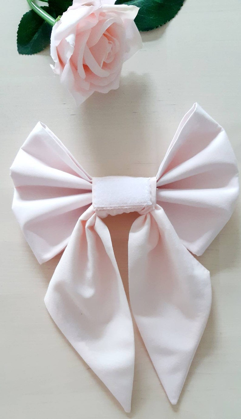 May include: A pale pink fabric bow with two long tails, tied with a white velcro strip.